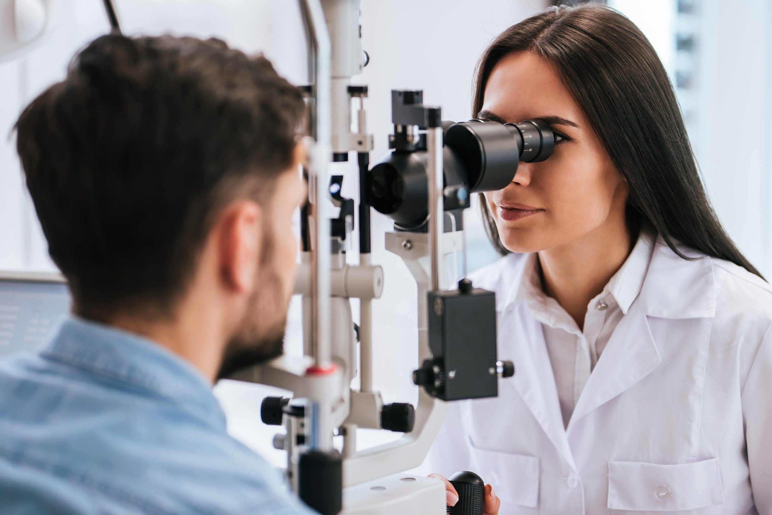 Female doctor ophthalmologist is checking the eye vision of young man in modern clinic.